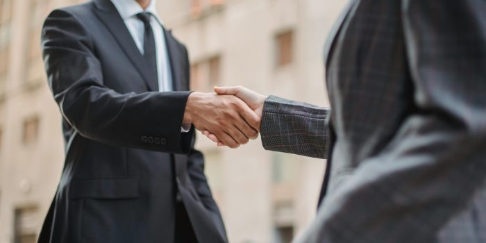 Business professionals greeting each other with a handshake outdoors, symbolizing partnership.